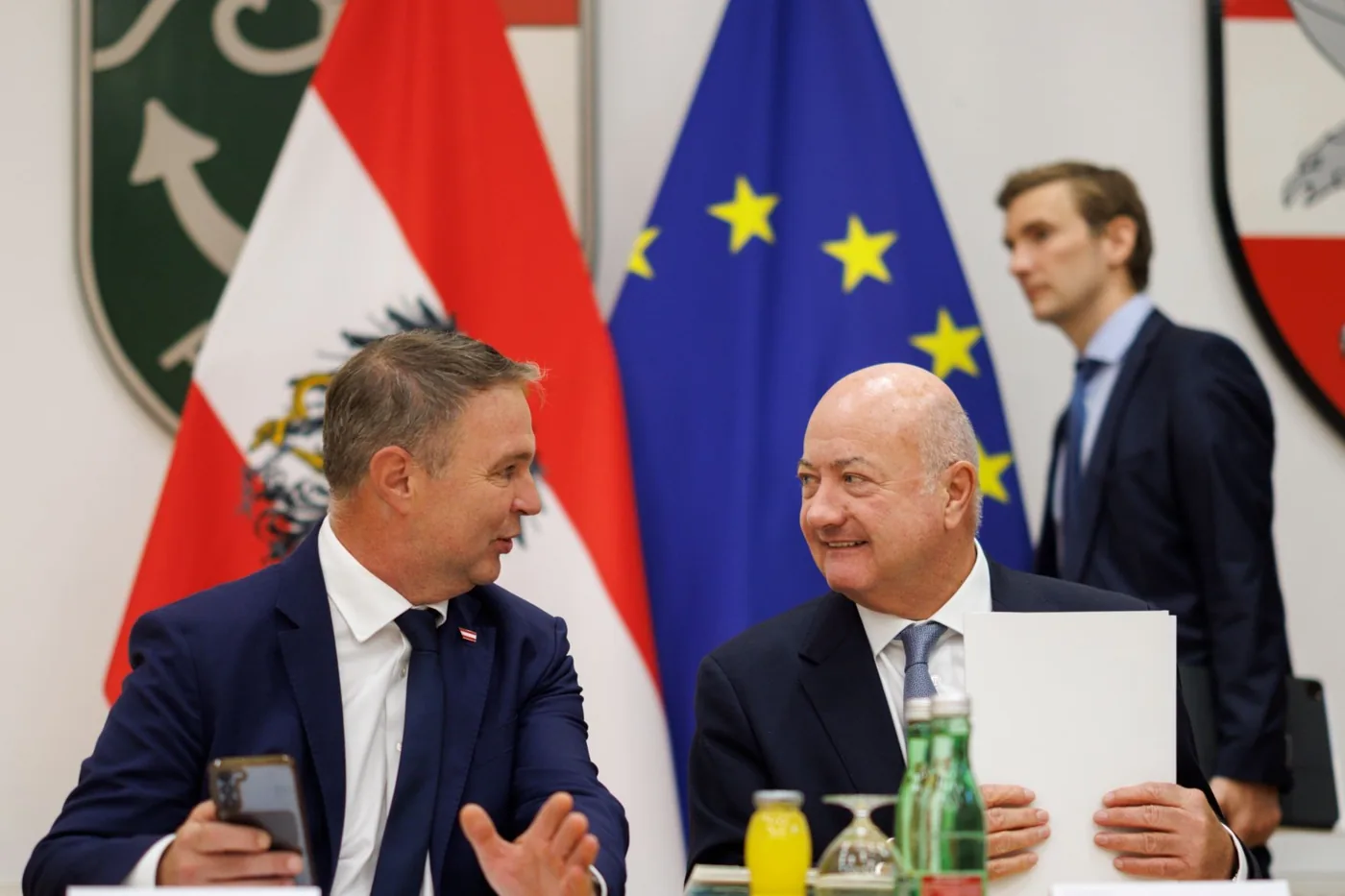 Bundeskanzler Stocker und Vizekanzler Babler am Tisch des Sommerministerrats, davor die österreichische und die europäische Fahne